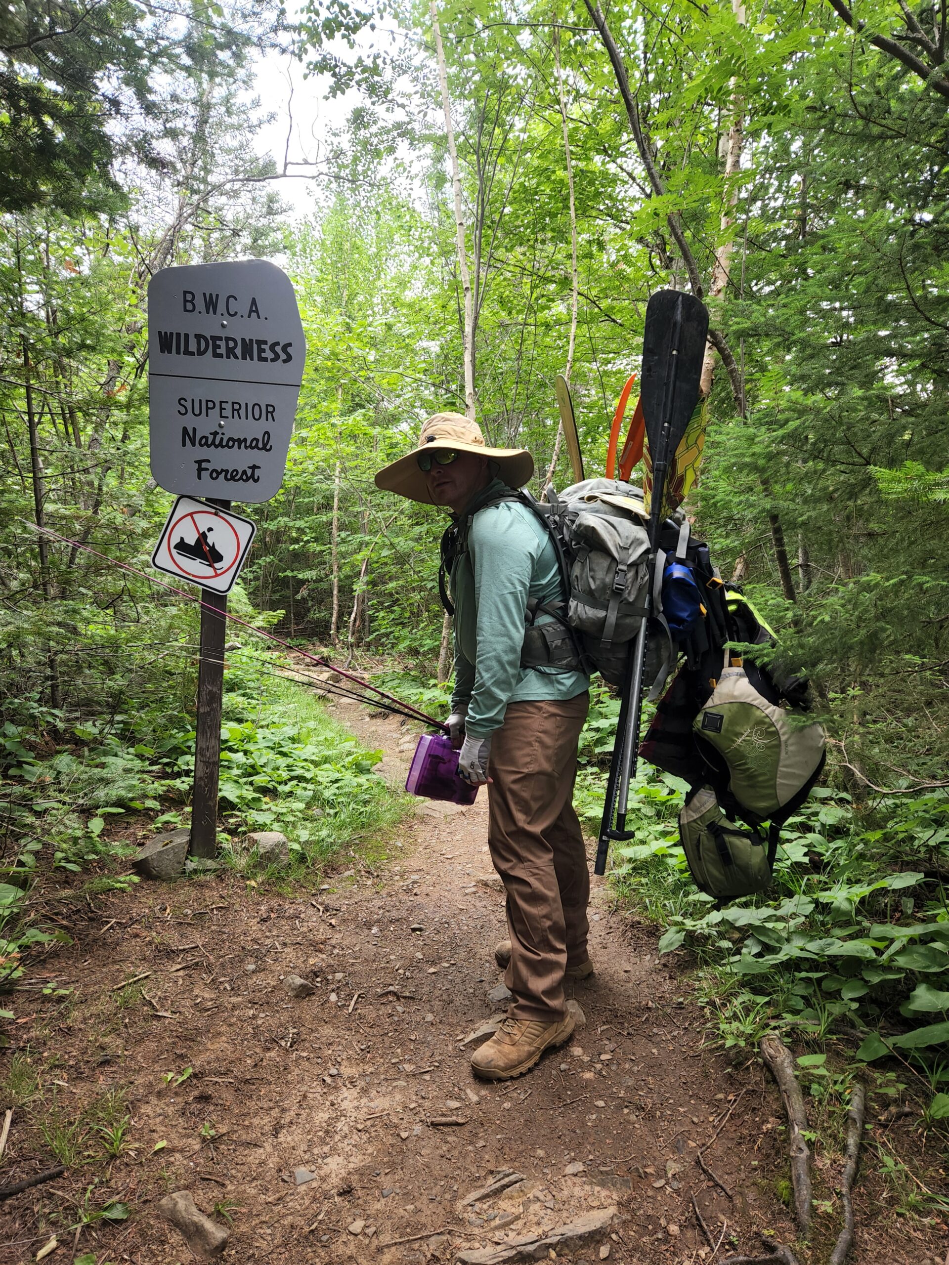 Tim loaded up with his large backpack with paddles and lifejacket hanging off it getting ready to portage through the Boundary Waters Canoe Area